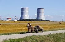 A man in a horse drawn carriage travels on a road, with Belarus's first nuclear plant in the background near Astravets, Belarus, Friday, Aug. 7, 2020.