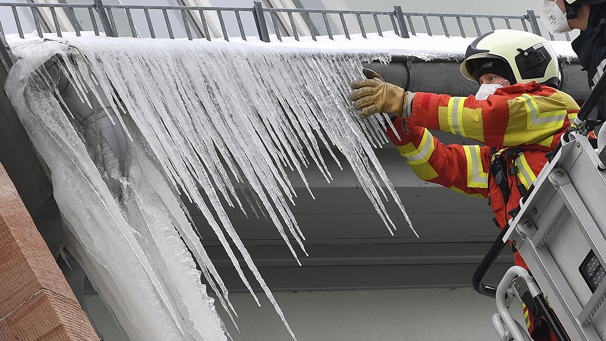 Firefighters break large icicles from the gutter of a house in the city centre of Erfurt, Germany, Thursday, Feb.11, 2021. 