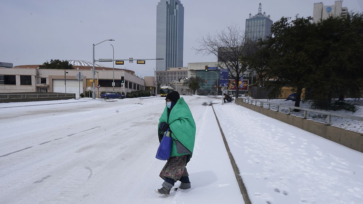 A woman wrapped in a blanket crosses the street near downtown Dallas, Tuesday, Feb. 16, 2021.