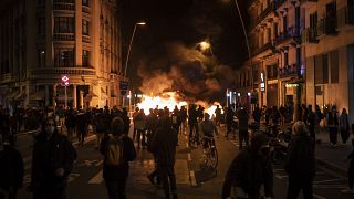 People gather next to a burning barricade during clashes after a protest condemning the arrest of rap singer Pablo Hasél in Barcelona, Spain, Wednesday, Feb. 17, 2021.