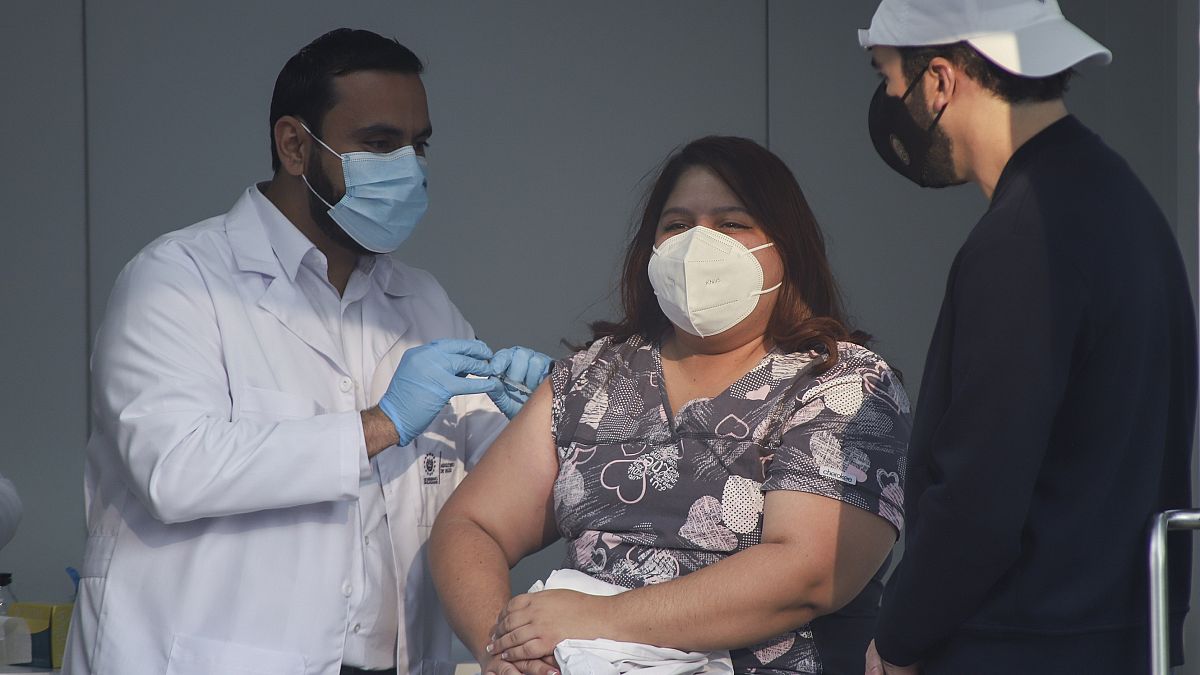 El ministro de Salud de El Salvador, Francisco Alabi, procede a vacunar a una enfermera ante la mirada atenta del presidente, Nayib Bukele.