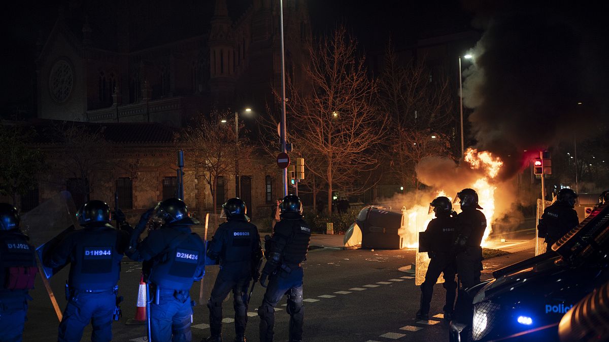 Police officers take position next to a burning barricade during clashes following a protest condemning the arrest of rap singer Pablo Hasél in Barcelona, Spain, Feb.18, 2021.