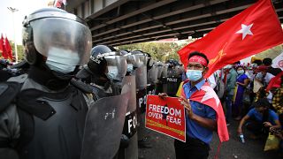 An anti-coup protester holds a poster as he stands in front of riot police in Yangon, Myanmar on Friday