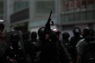 A Hong Kong police officer aiming his weapon at demonstrators on a pedestrian bridge in 2019.