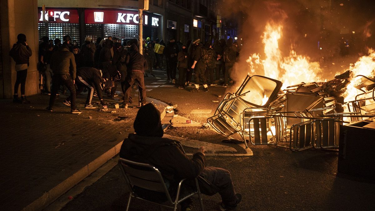A man sits on a chair in front of a burning barricade during a protest condemning the arrest of rap singer Pablo Hasél in Barcelona, Spain, Friday, Feb. 19, 2021.