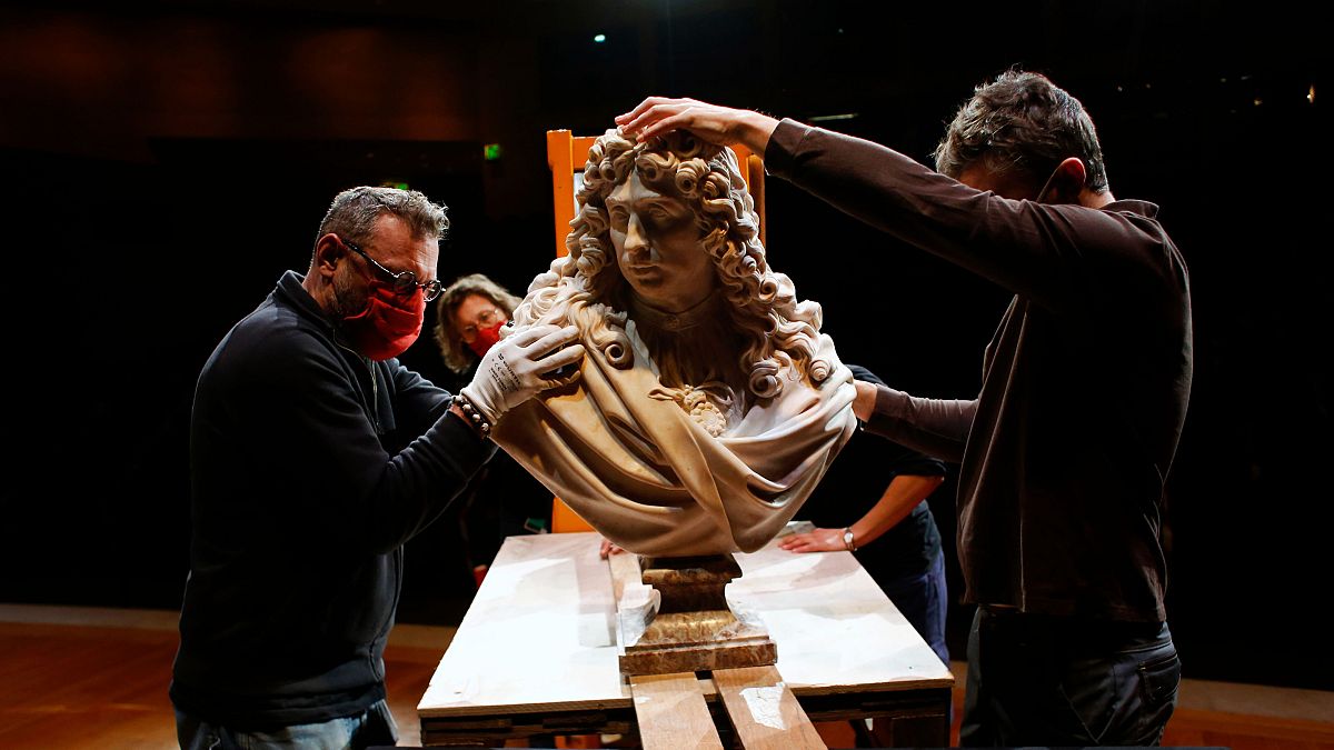 Workers handle a bust of Charles Le Brun by French sculptor Antoine Coysevox, in the Louvre museum
