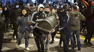 Demonstrators carry a rubbish bin to throw it agains police officers protecting a national police station during clashes following a protest condemning the arrest of a rapper.