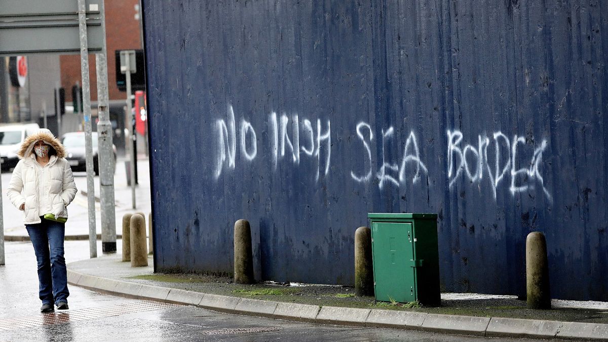 A woman walks past past graffiti with the words 'No Irish Sea Border' in Belfast city centre, Northern Ireland, Wednesday, Feb. 3, 2021. 