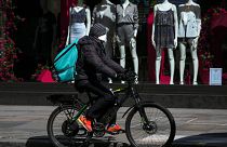 A food delivery rider wears a mask as he rides in a deserted Regent Street, during lockdown to protect against the Coronavirus outbreak, in London, Tuesday, April 14, 2020.