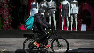 A food delivery rider wears a mask as he rides in a deserted Regent Street, during lockdown to protect against the Coronavirus outbreak, in London, Tuesday, April 14, 2020.