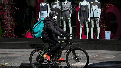 A food delivery rider wears a mask as he rides in a deserted Regent Street, during lockdown to protect against the Coronavirus outbreak, in London, Tuesday, April 14, 2020.
