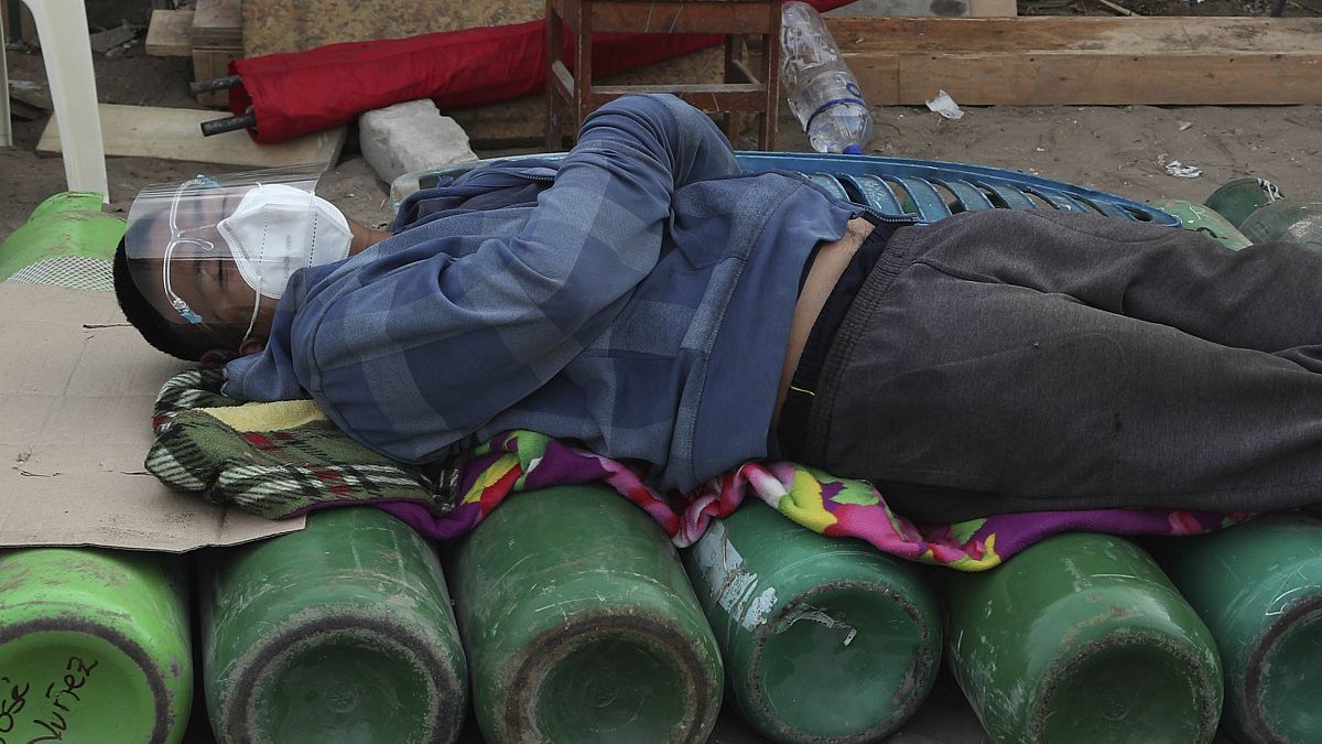 Un hombre duerme sobre bombonas de oxígeno vacías, a la espera de que abra una tienda, en Lima.