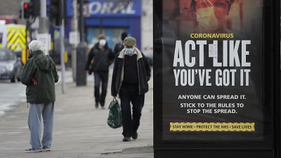 FILE: Pedestrians pass a sign on a bus stop in West Ealing in London, Thursday, Feb. 25, 2021.