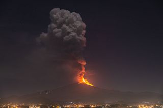 Flames and smoke billowing from a crater, as seen from the southern side of the Mt Etna volcano, tower over the city of Pedara, Sicily, Wednesday night, Feb. 24, 2021.