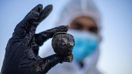 An Israeli soldier wearing a full protective suit holds a piece of tar from an oil spill in the Mediterranean Sea.