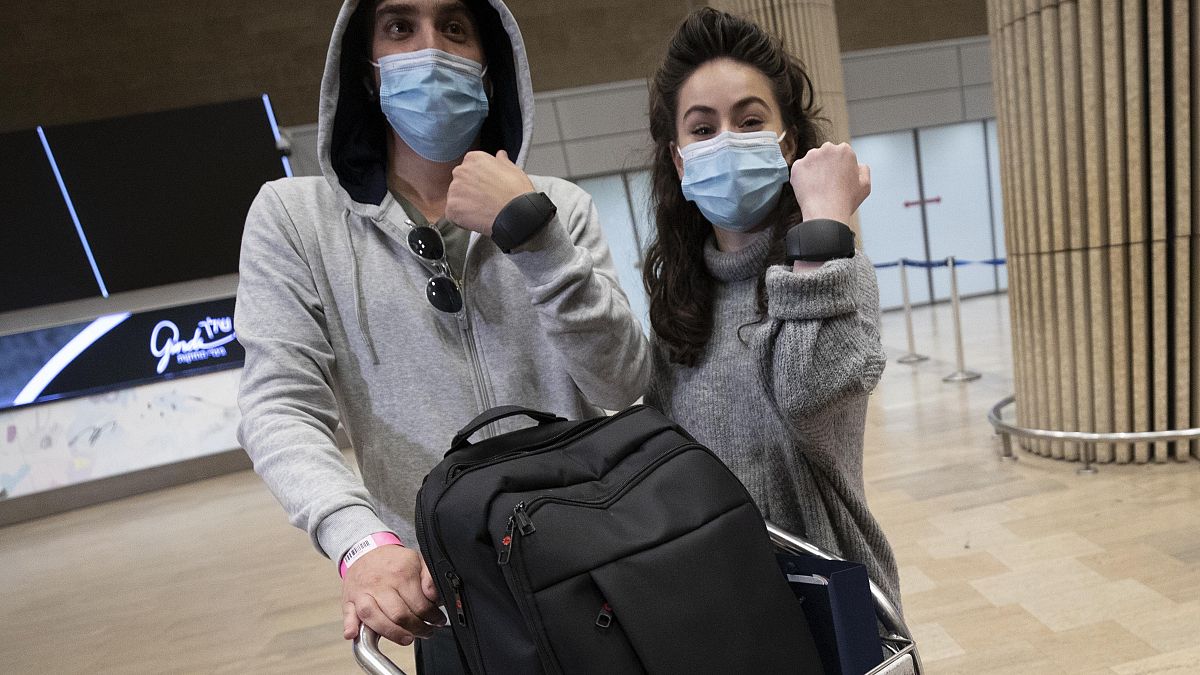 Israeli travelers hold up electronic monitoring bracelets they are required to wear after returning from abroad at the Ben Gurion airport near Tel Aviv