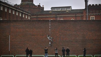 Members of the public pause to look at an artwork bearing the hallmarks of street artist Banksy on the side of Reading Prison in Reading, west of London
