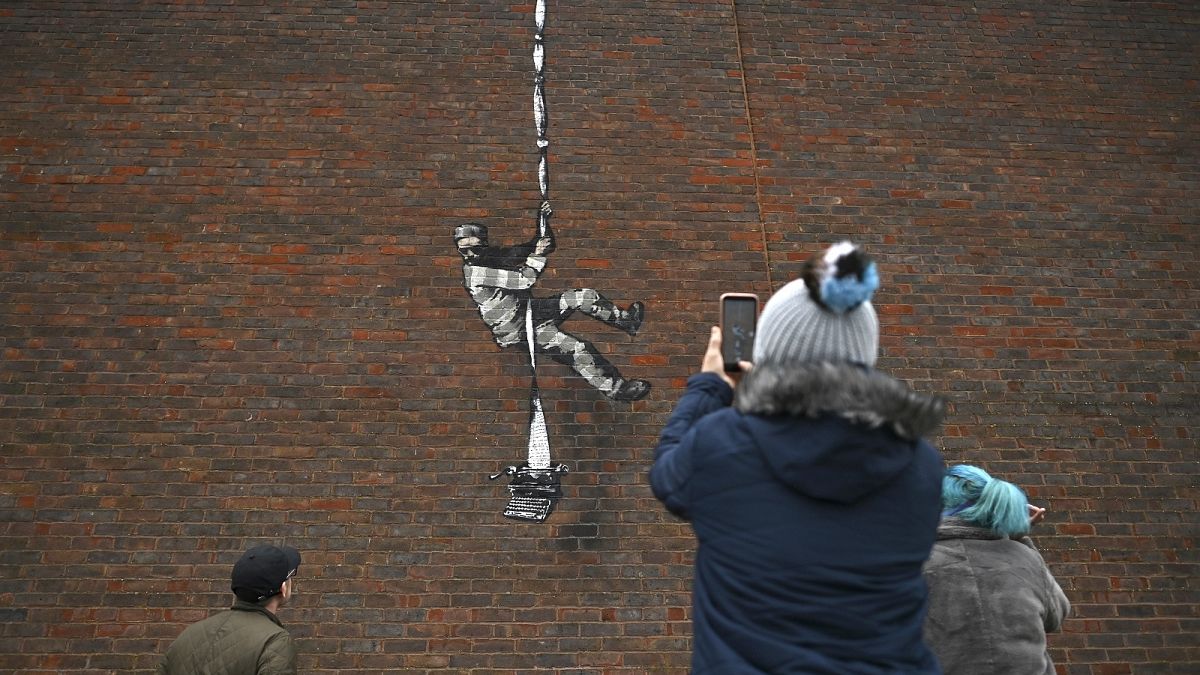 Members of the public pause to look at an artwork by street artist Banksy on the side of Reading Prison in Reading, west of London.