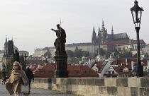 A woman wearing a face mask walks across the medieval Charles Bridge in Prague.