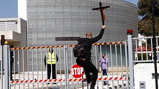 A protestor holding a cross climbs a gate outside Cyprus' national broadcasting building, during a protest against the country’s entry into this year’s Eurovision song contest