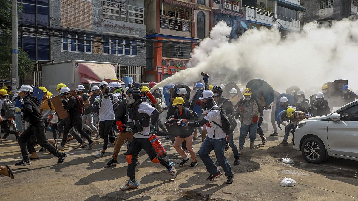 In this March 3, 2021, file photo, anti-coup protesters run as one of them discharges a fire extinguisher to counter the impact of tear gas fired by riot policemen in Yangon.