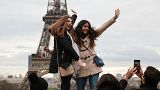Young people pose for pictures in front of Paris' Eiffel Tower.