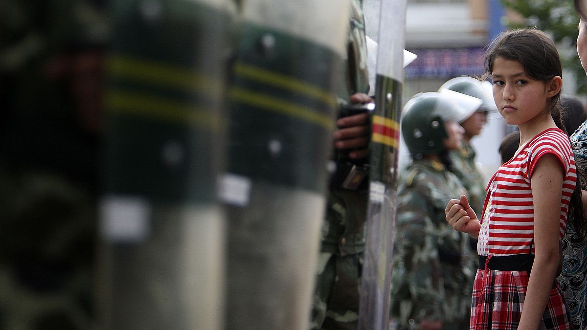 فتاة من الإيغور أمام عناصر من قوات الأمني الصينية المنتشرة في مدينة أورومتشي بمقاطعة شينجاينغ