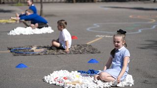 Children at Seymour Road Academy sit in designated areas in the playground during the coronavirus outbreak in Manchester, England, Wednesday May 20, 2020.