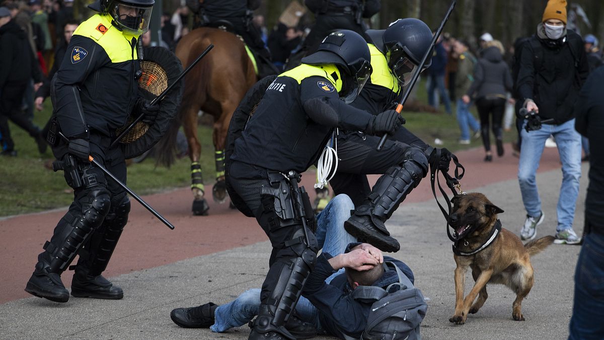 Dutch riot police kick a man during a demonstration to protest government policies including the curfew, lockdown and coronavirus related restrictions in The Hague.