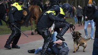 Dutch riot police kick a man during a demonstration to protest government policies including the curfew, lockdown and coronavirus related restrictions in The Hague.