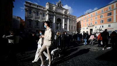 People enjoy a sunny day by the Trevi Fountain in downtown Rome on March 13, 2021 before the government tightens restrictions across most of the country from March 15.