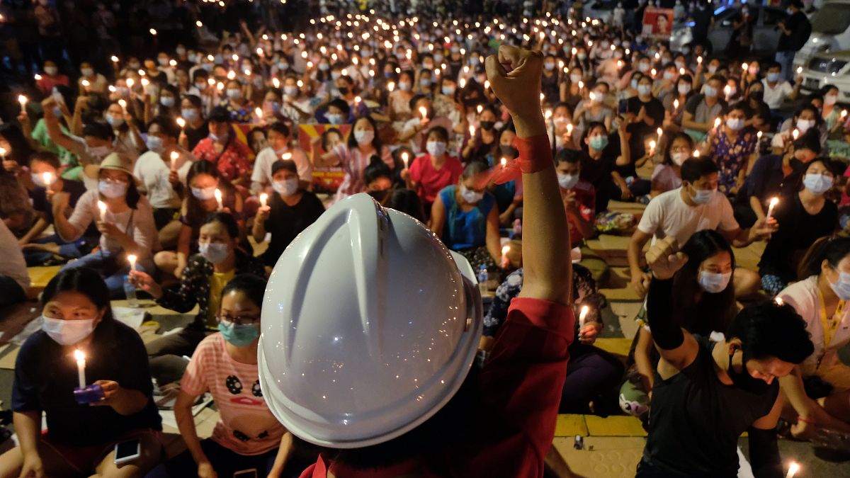 An anti-coup protester raises his hand with clenched fist in front of a crowd during a candlelight night rally in Yangon, Myanmar Sunday, March 14, 2021.