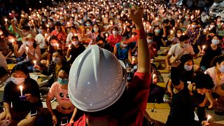 An anti-coup protester raises his hand with clenched fist in front of a crowd during a candlelight night rally in Yangon, Myanmar Sunday, March 14, 2021.