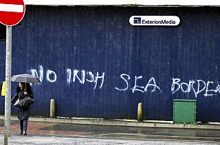 A woman walks past past graffiti with the words 'No Irish Sea Border' in Belfast city centre, Northern Ireland, Wednesday, Feb. 3, 2021.