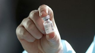 Pfizer/BioNTech aşı şişesini gösteren bir sağlık çalışanı