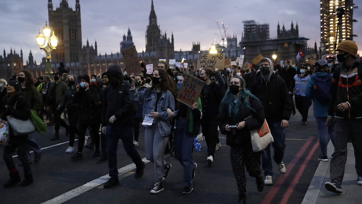 People hold signs as they march across Westminster bridge outside the Parliament during a march to reflect on the murder of 33 year old marketing executive, Sarah Everard.
