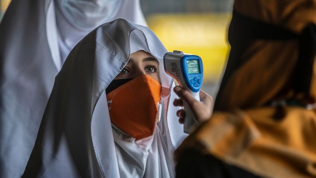 Un membro del personale controlla la temperatura alle  studentesse, che tornano sui banchi di scuola a Srinagar, nel Kashmir controllato dall'India