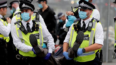 olice officers with face masks carry a protestor away during an Extinction Rebellion climate change protest at Parliament Square in London.