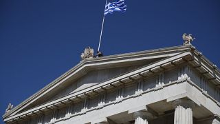 A worker adjusts the Greek flag atop of the old National Library building in Athens.