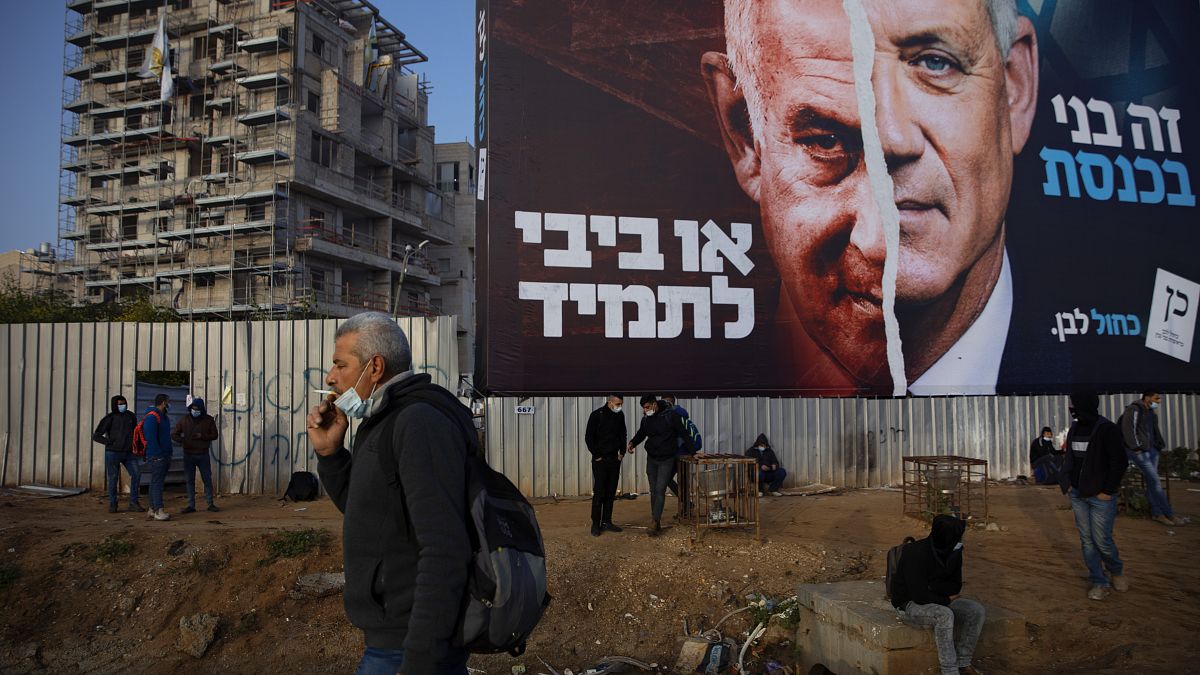 فلسطينيون ينتظرون المواصلات تحت لوحة إعلانية لحملة الانتخابات الإسرائيلية. 2021/03/14