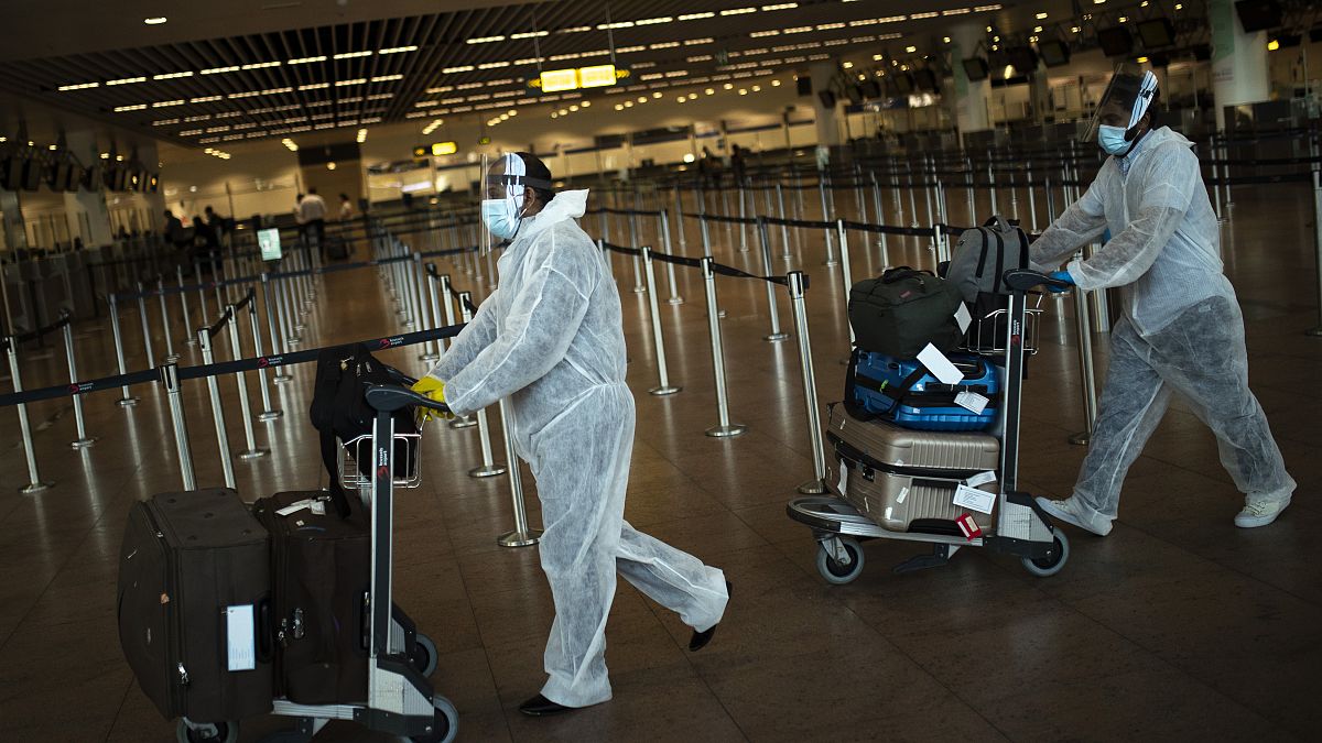 FILE - In this July 29, 2020 file photo, passengers wearing full protective gear push their luggage in the departure hall of Zaventem international airport, Belgium