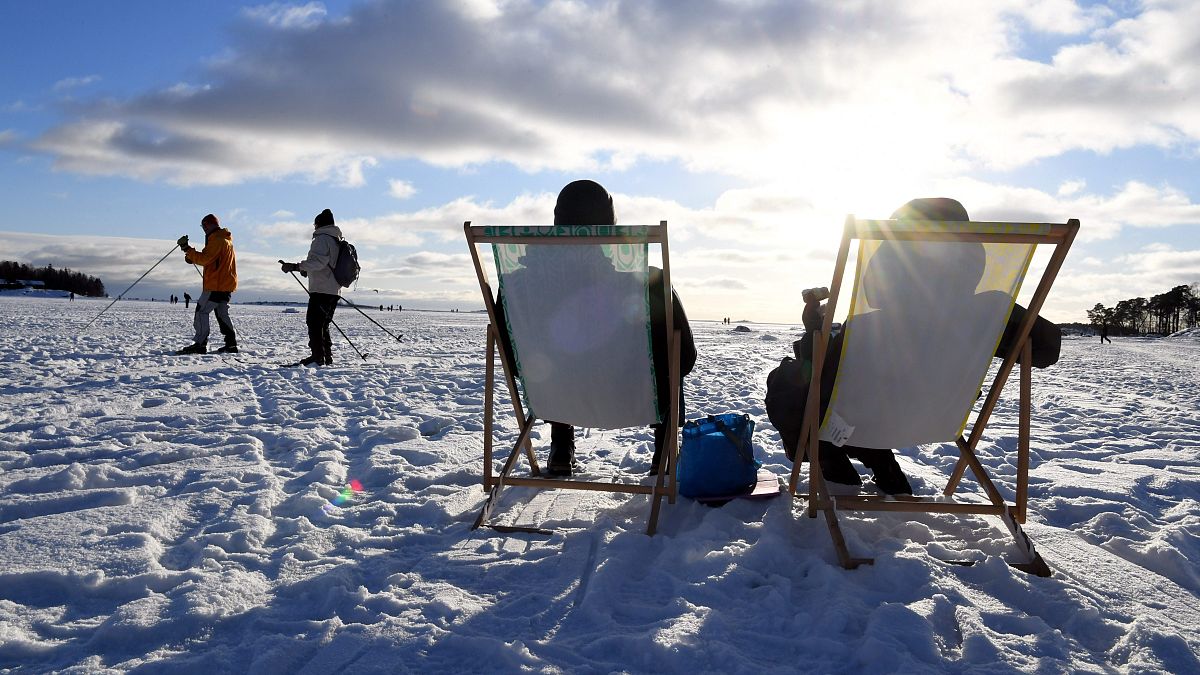 أشخاص يستمتعون بأشعة الشمس في الواجهة البحرية الجليدية في هلسنكي، فنلندا.