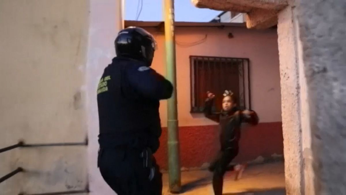Un policía apunta con un arma a una niña en un operativo para hacer cumplir las medidas contra la COVID-19.