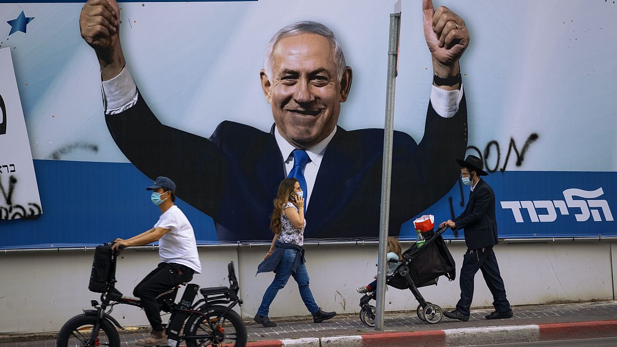 People pass an election campaign billboard for the Likud party that shows a portrait of its leader Prime Minister Benjamin Netanyahu, in Ramat Gan, Israel, , March 21, 2021