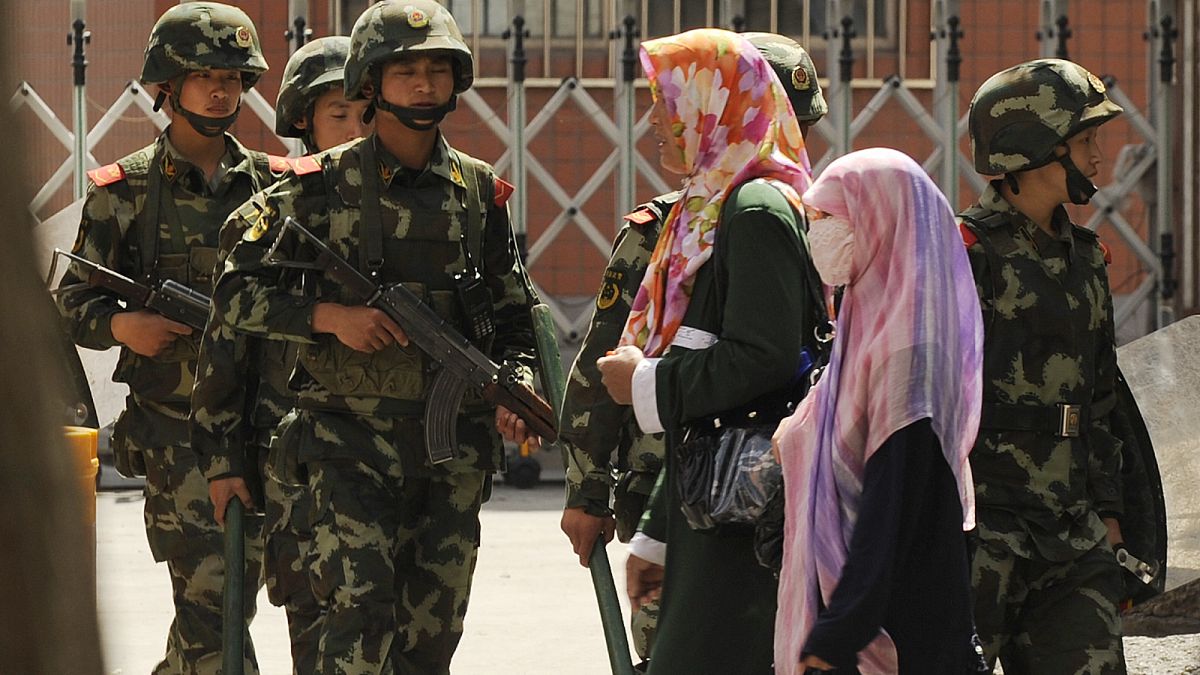 نساء مسلمات من الإيغور يسرن أمام الشرطة الصينية شبه عسكرية في أحد شوارع أورومتشي، عاصمة منطقة شينجيانغ الصينية.