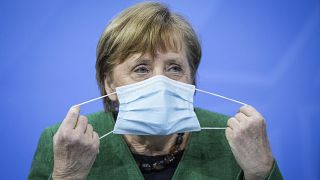 German Chancellor Angela Merkel removes her mask at the start of a press conference in Berlin, Tuesday, March 23, 2021.