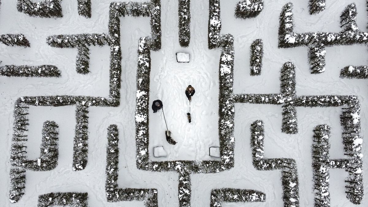 Menschen spazieren mit ihren Hunden in einem schneebedeckten Gartenlabyrinth in Gelsenkirchen, 10.02.2021