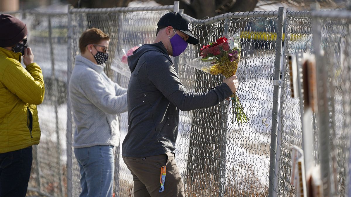 Kiefer Johnson places a bouquet of flowers into a makeshift fence put up around the parking lot outside a King Soopers grocery store where a mass shooting took place.