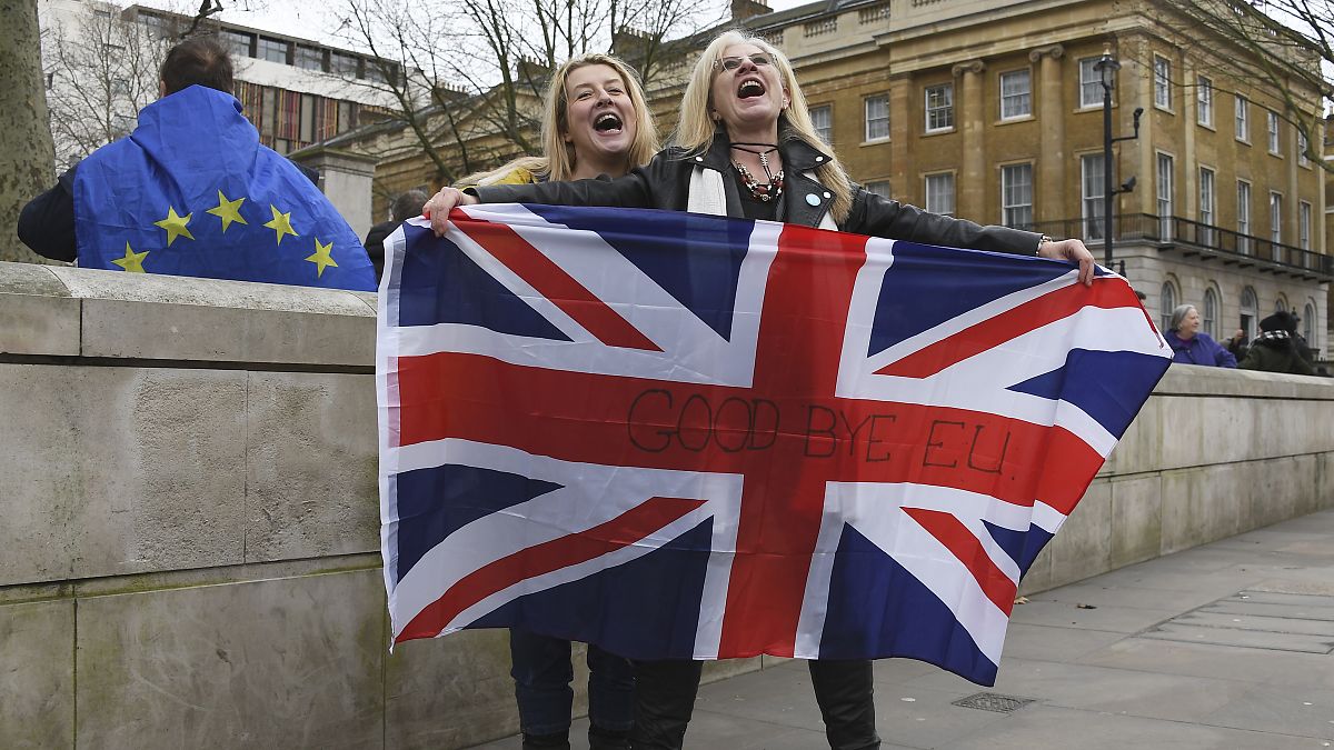 Brexit supporters hold the Union Jack with a text reading "Goodbye EU" as they celebrate next to a person wearing the EU flag in London, Friday, Jan. 31, 2020.