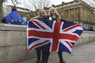 Brexit supporters hold the Union Jack with a text reading "Goodbye EU" as they celebrate next to a person wearing the EU flag in London, Friday, Jan. 31, 2020.